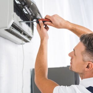 A man from Cairns is fixing an air conditioner on a wall using his expertise at Hielscher Electrical.