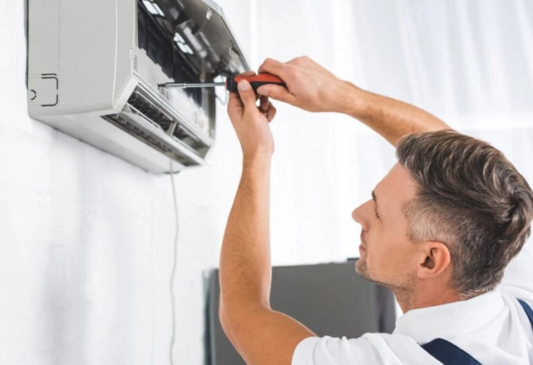 A man from Cairns is fixing an air conditioner on a wall using his expertise at Hielscher Electrical.