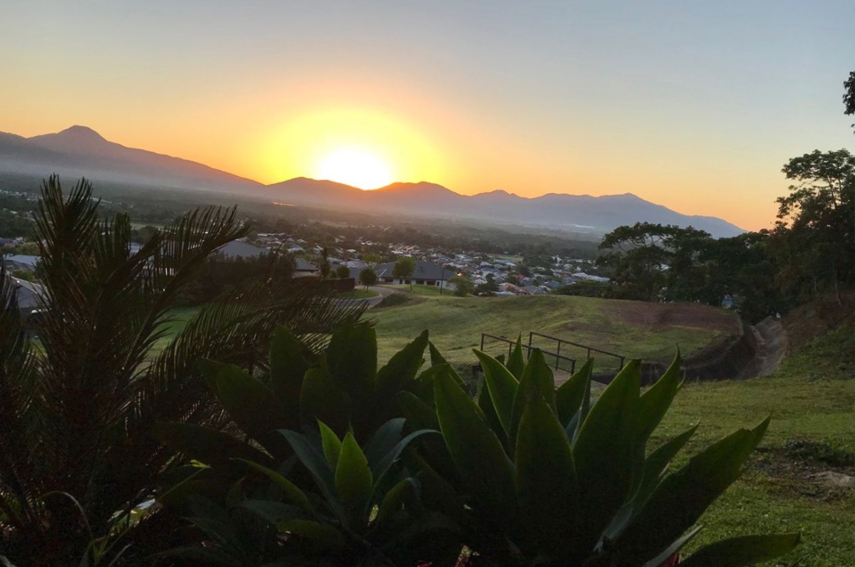 A view of the sun setting over a garden and mountains, with solar panels harnessing solar power in the scene.