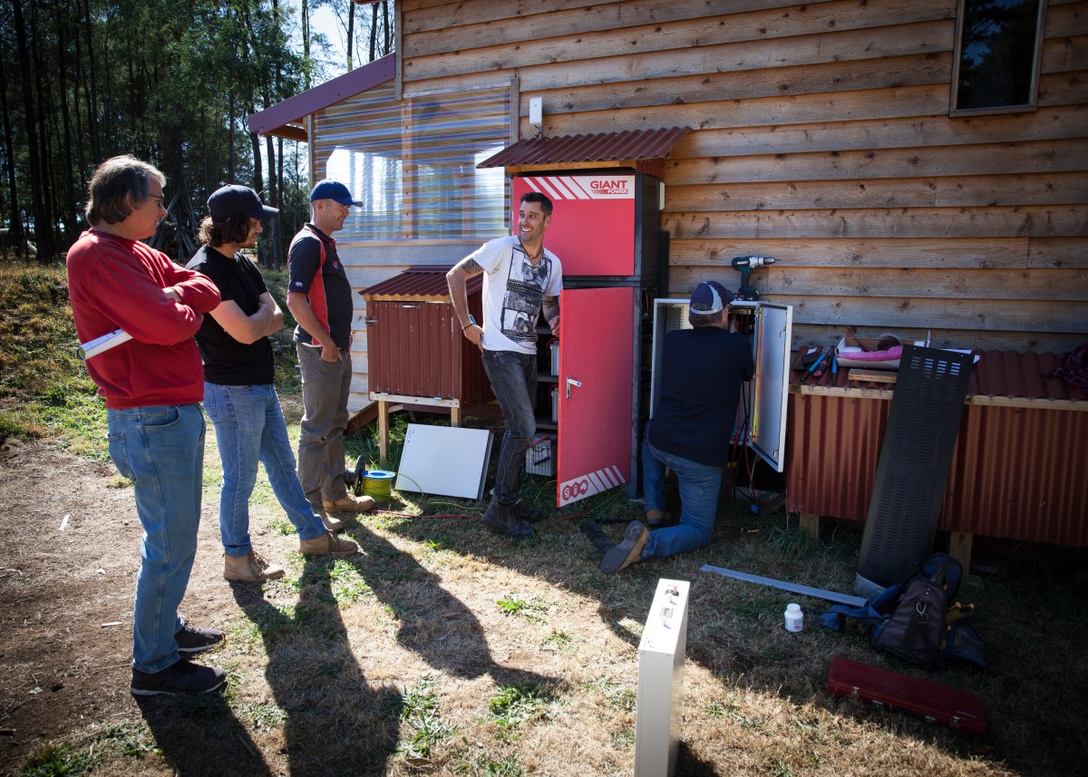 A group of people standing in front of a house powered by solar panels.