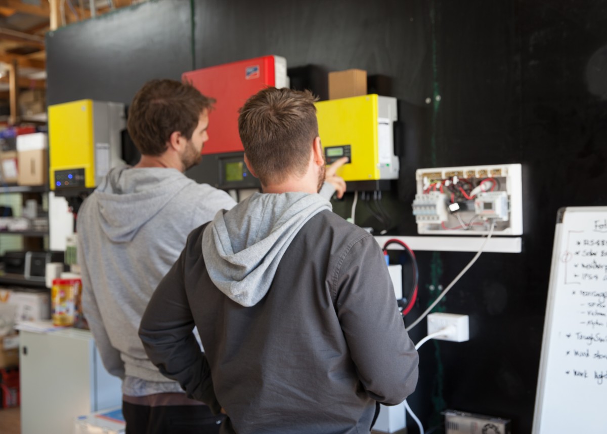 Two men standing in front of a blackboard discussing solar panels in a warehouse.