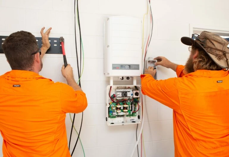Two men in orange shirts working on a solar power electrical system.