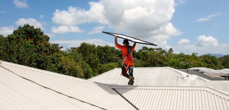 A man holding a solar surfboard on top of a roof, promoting Solar Power.