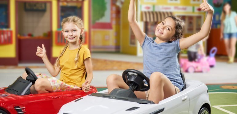 Two girls in toy cars exploring a toy store.