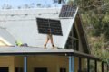 A man standing on the roof of a house harnessing solar power with solar panels in Cairns.