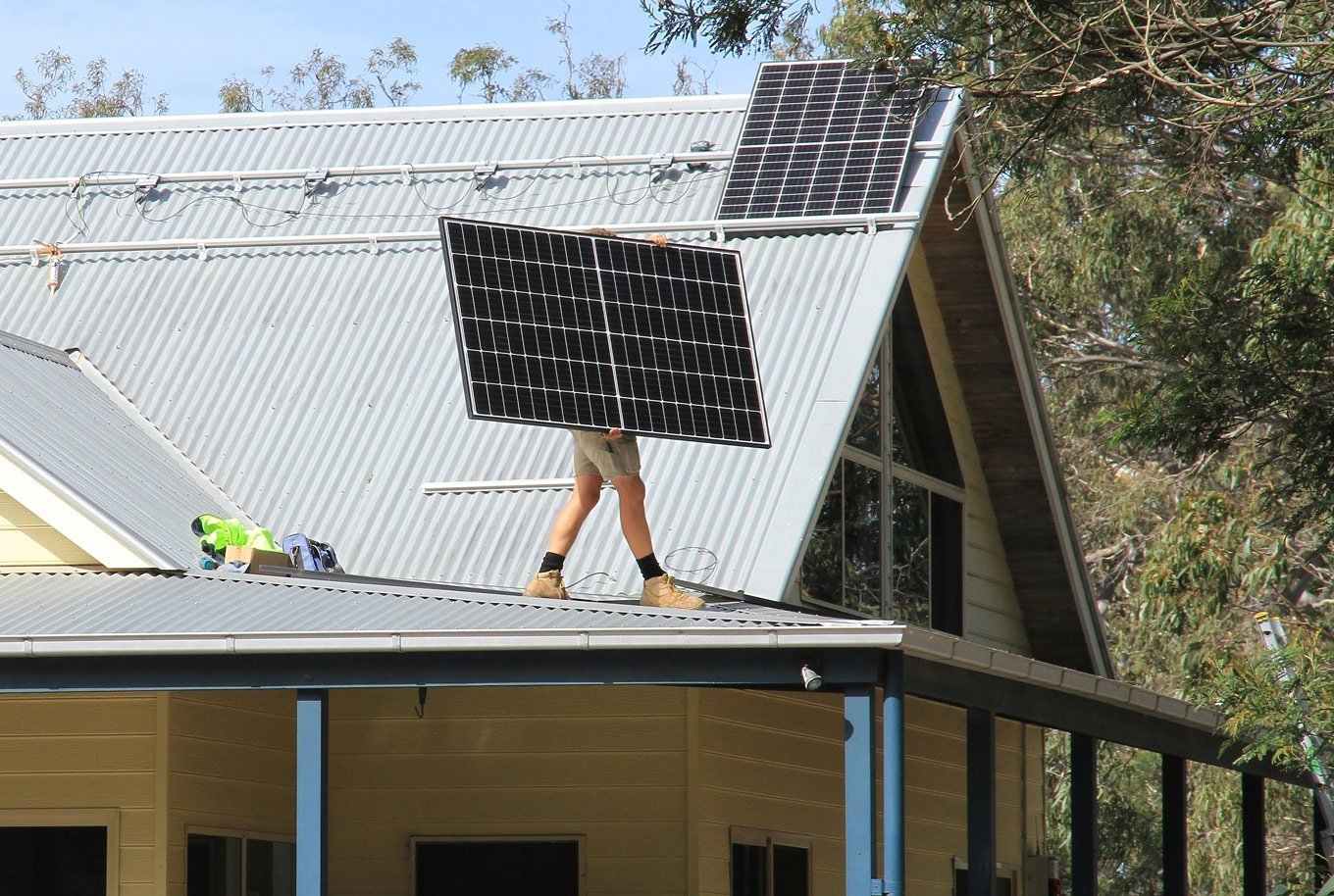 A man standing on the roof of a house harnessing solar power with solar panels in Cairns.