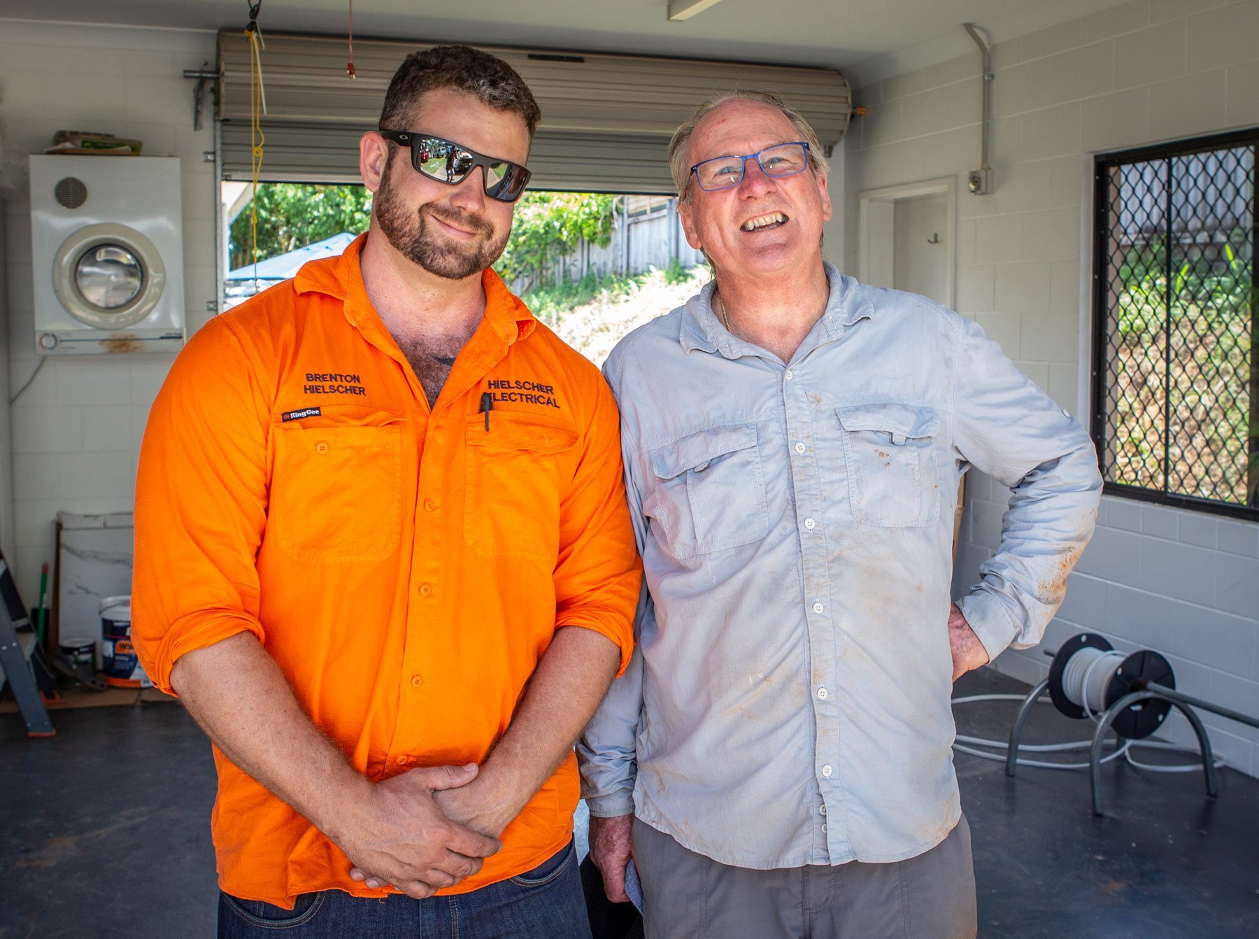 Two men standing next to each other in a garage filled with solar panels.