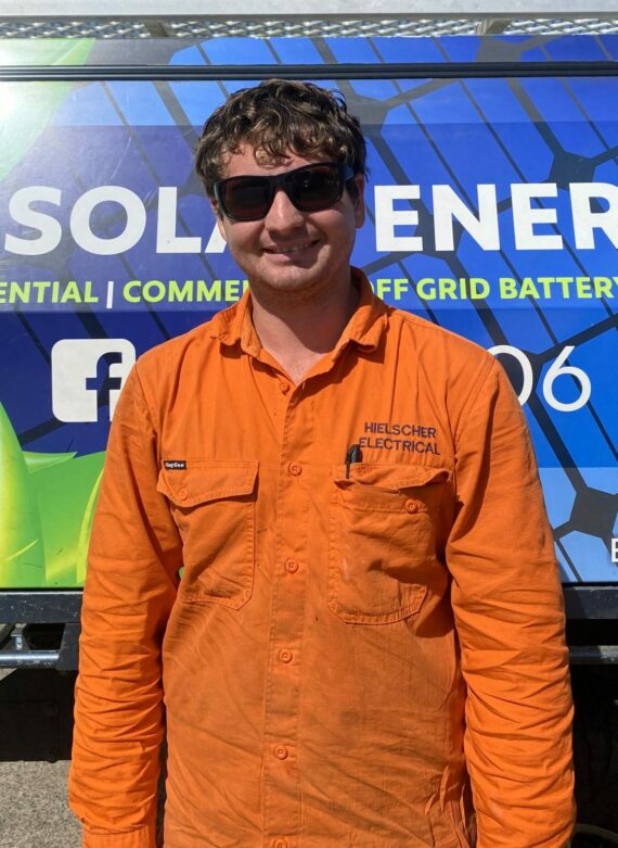 A man in an orange shirt standing in front of a Hielscher Electrical solar truck.