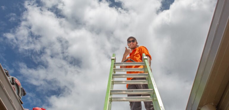 A man from Hielscher Electrical standing on a ladder installing solar panels.