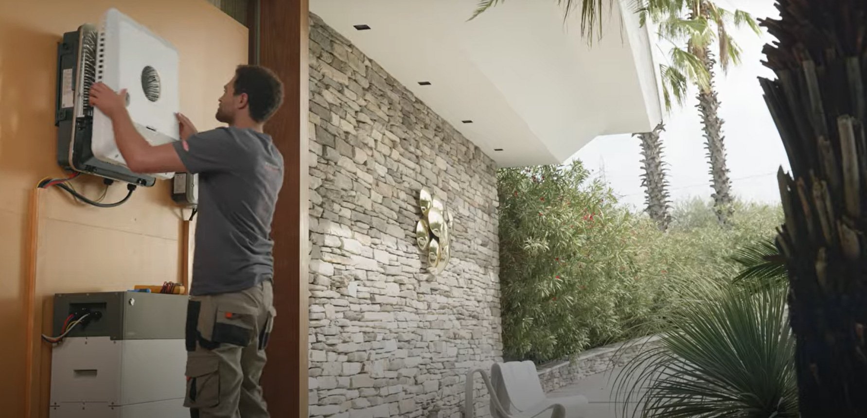 A man, representing Hielscher Electrical, installing a solar-powered air conditioner on a wall.