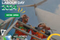 An advertisement for "hielscher electrical" showing two engineers working on a wind turbine in Queensland, with text announcing open business hours for Labour Day 2024.