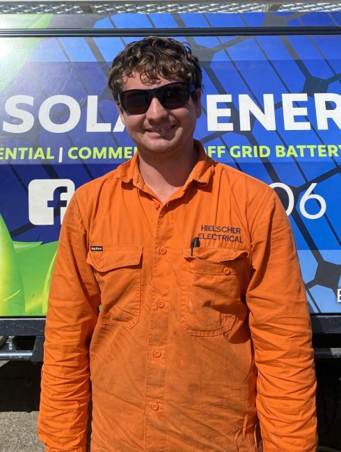 A man in an orange shirt standing in front of a Hielscher Electrical solar truck.