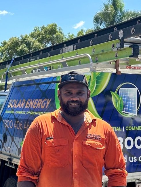 Man and his team in orange shirts standing in front of a van with solar energy service advertisements, under a sunny sky.